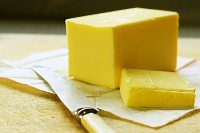 Block of butter, cut, on old chopping board, with bone-handled knife.